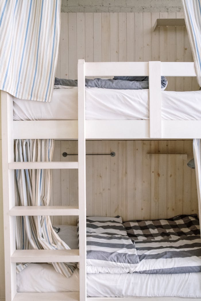 digital-01 Minimalist bunk bed with striped bedding in a cozy, wooden-walled bedroom setting.